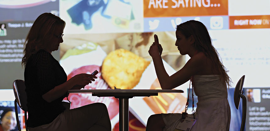 McDonald’s attendees check mobile devices in the Engagement Center with the social media mosaic LED wall in the background. Credit: McDonald’s Corporation
