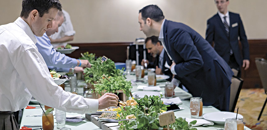 Attendees gather around a conference table to assemble a "Cut & Create Salad" with local greens and more.